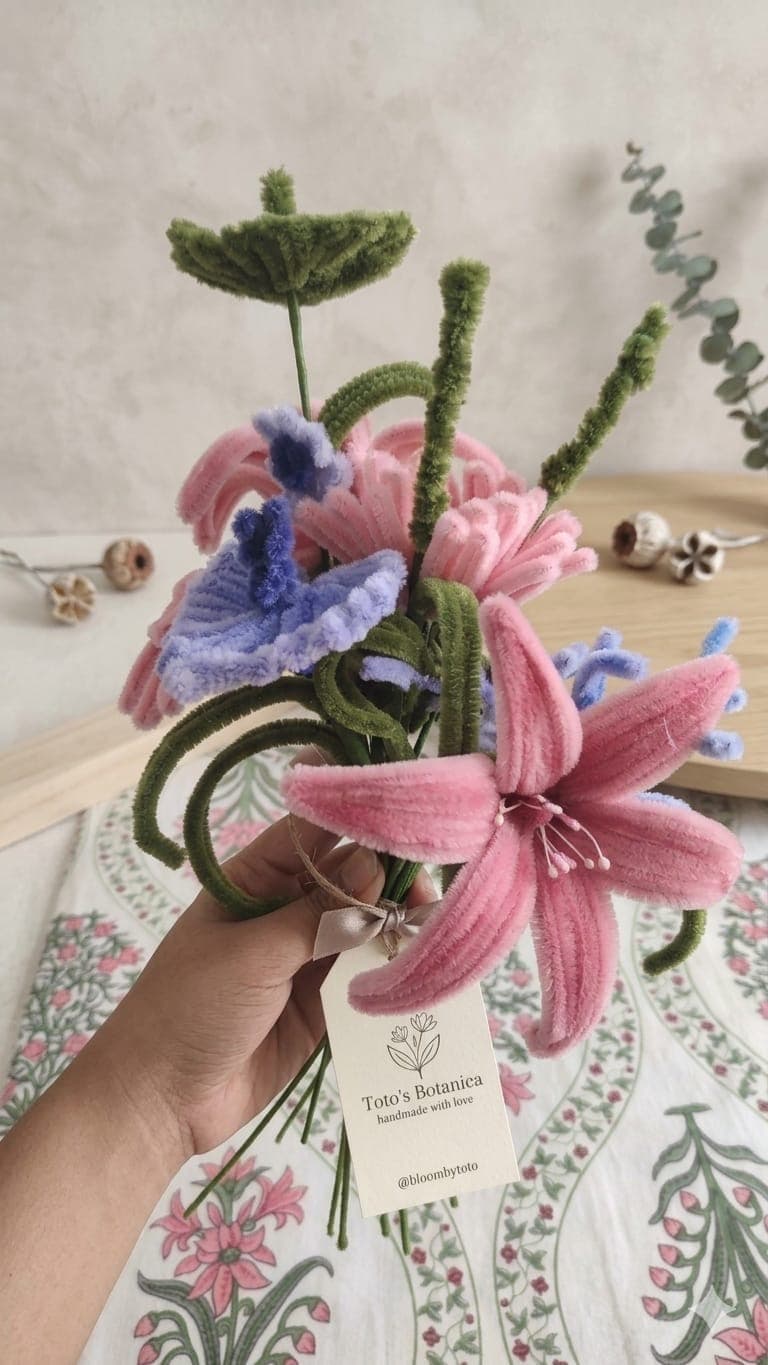 A crochet bouquet of pink lilies, blue bluebells, and curling green stems.